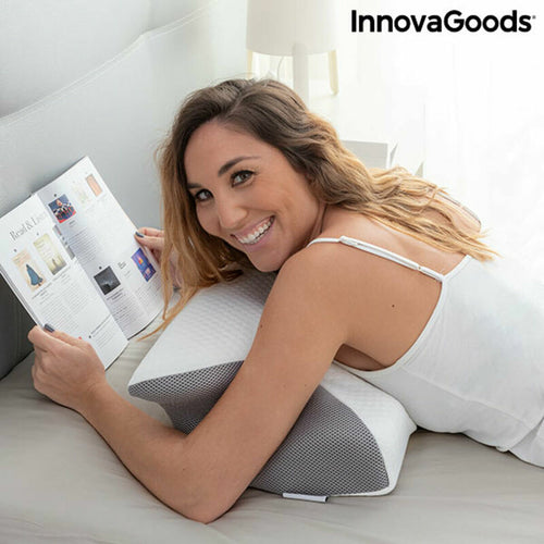 Woman reading a book while leaning on a white and grey contoured foam pillow on a bed. InnovaGoods logo in the corner.