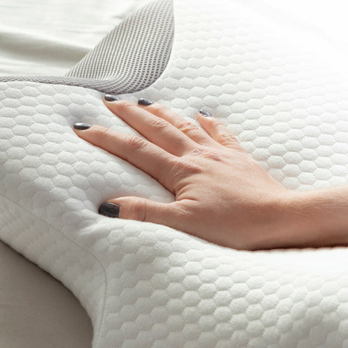 A hand presses into a white contoured fabric pillow with a hexagonal textured pattern and grey mesh trim.
