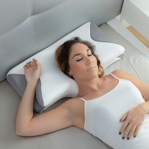 A woman sleeps on a white and grey contoured fabric pillow with a textured surface on a bed.